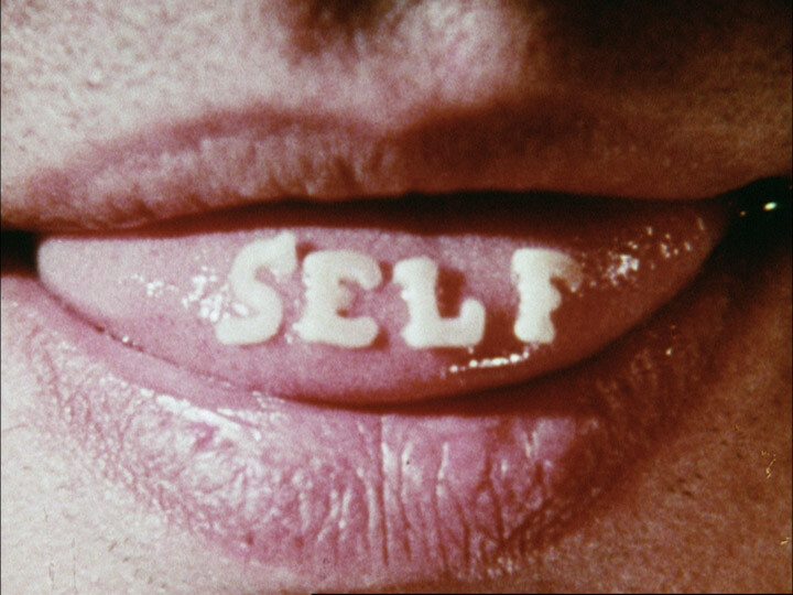 Lips parted to show the word "SELF" spelled in white letters on the tongue.