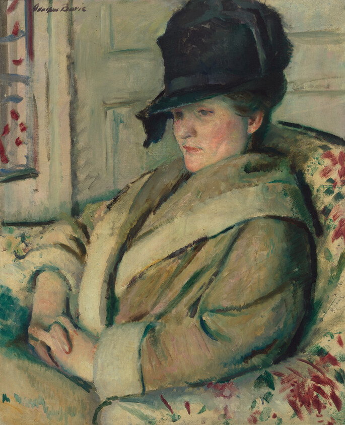 Woman in a dark hat and heavy coat sits with folded hands, gazing to the side.