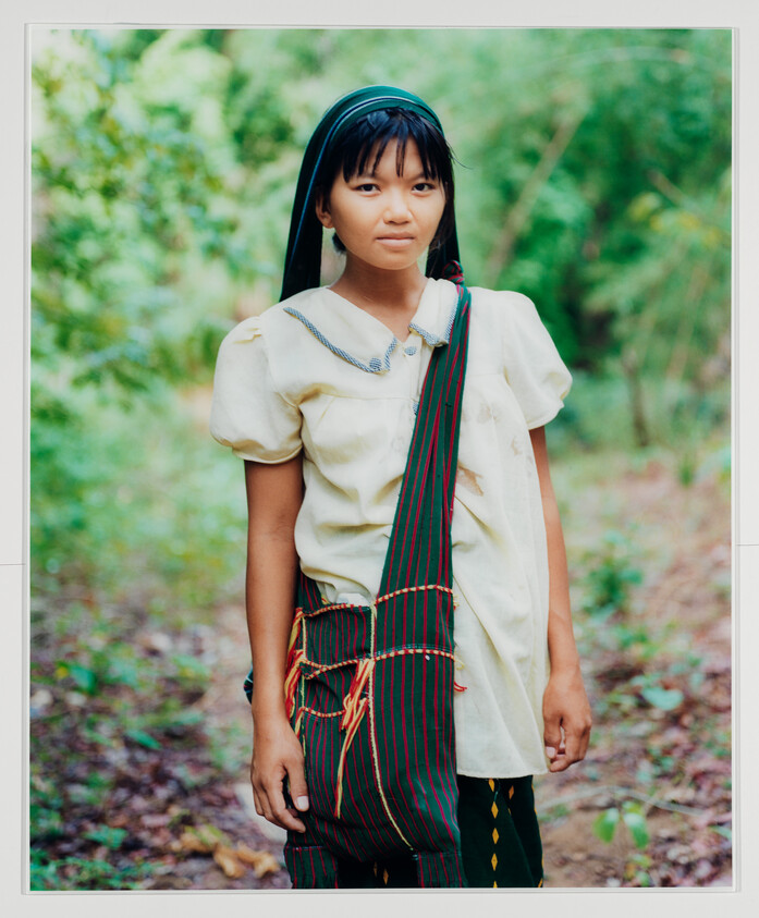 Young girl standing in forest wearing a headscarf and striped shoulder bag.