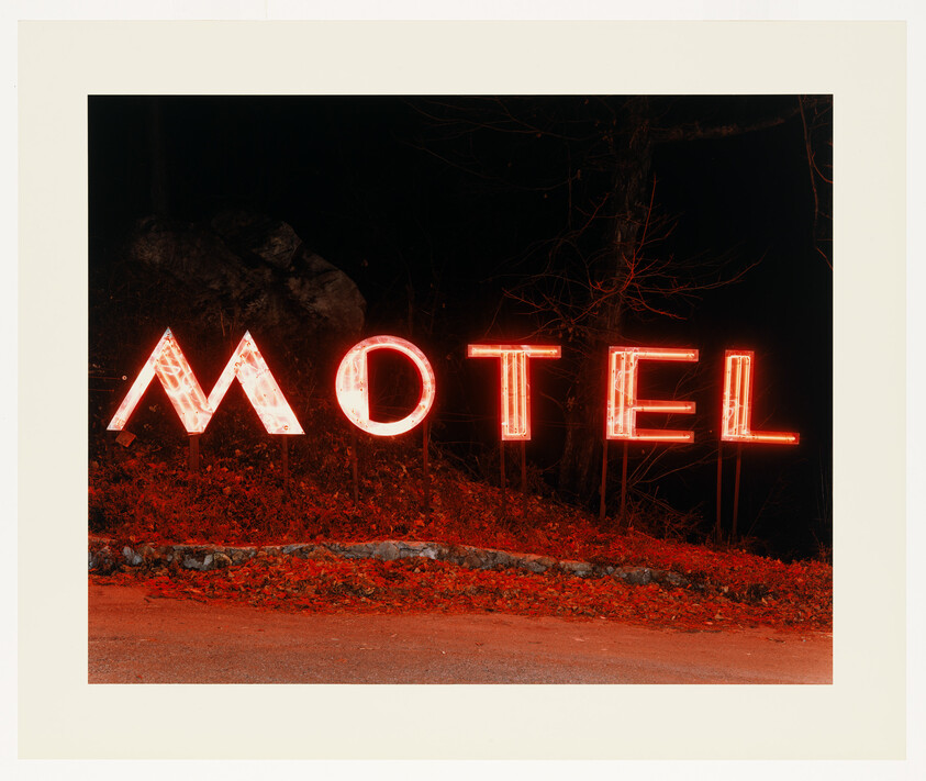 Bright red neon motel sign glowing at night beside a dark roadside embankment.
