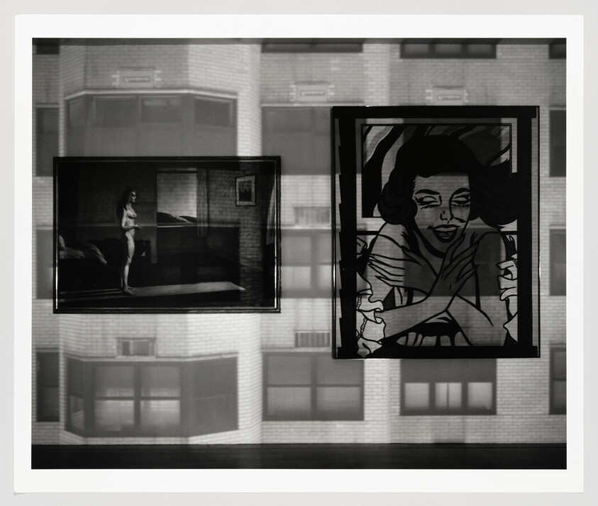 Two framed artworks hang in a window, one showing a nude figure and one a stylized woman.