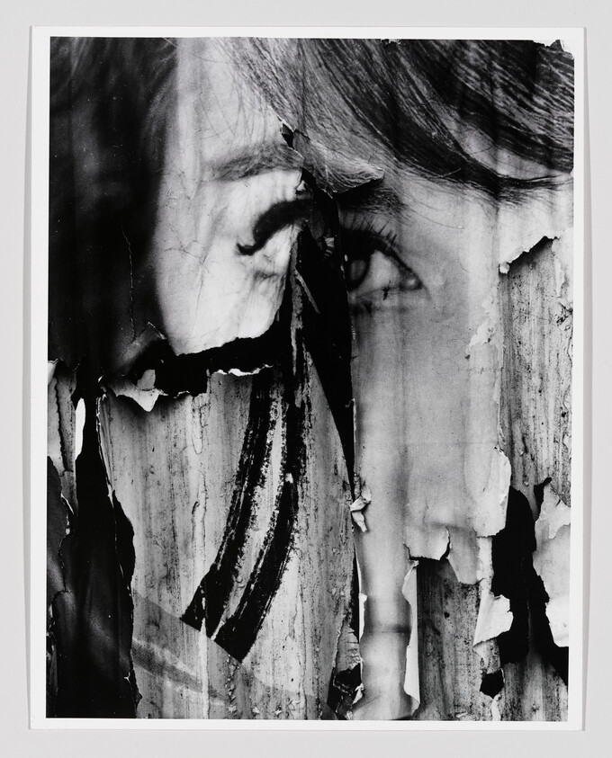A torn black-and-white poster of a woman's face peeling away from a weathered wall.