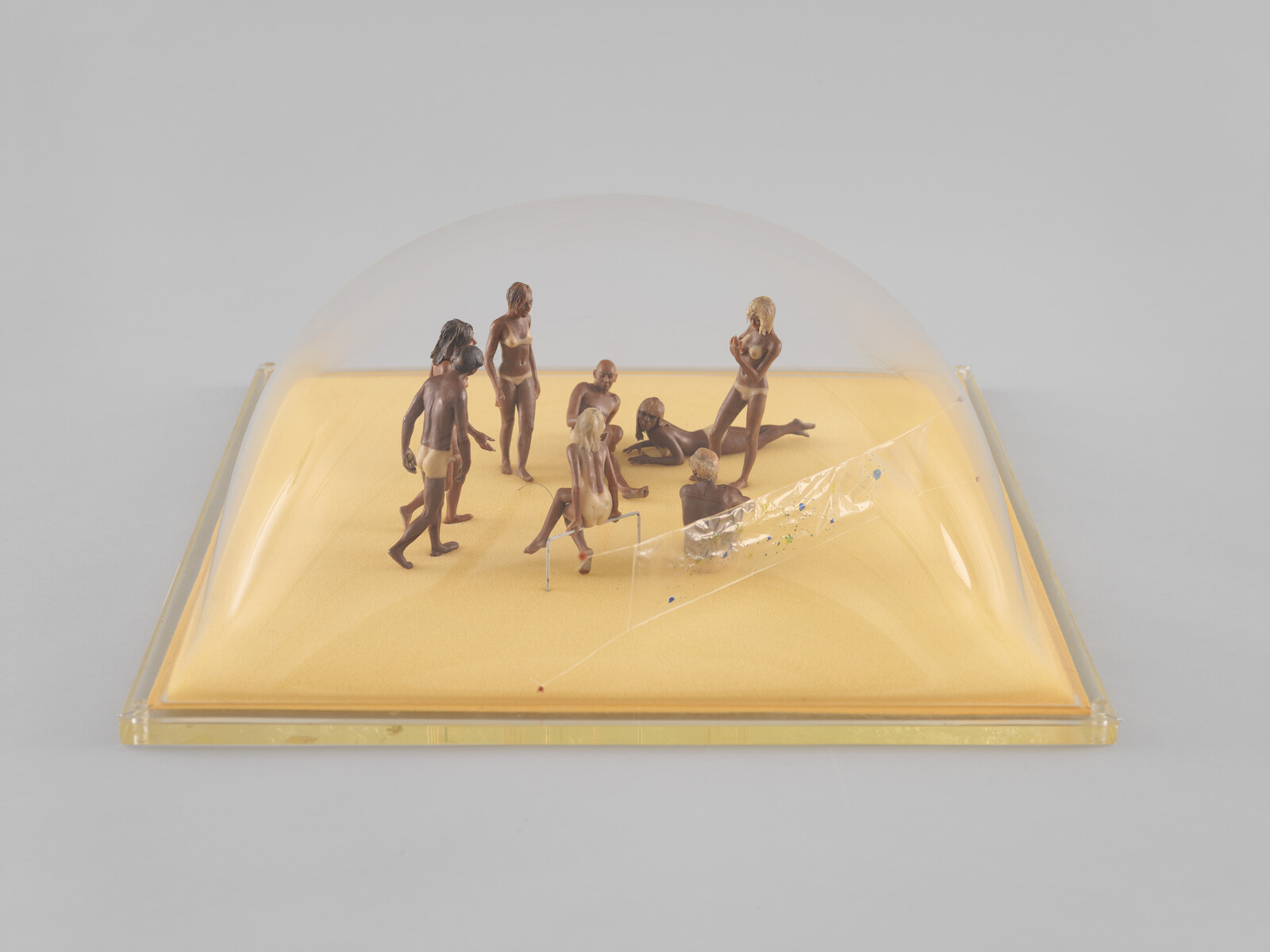 Small plastic figurines in swimwear gather on a yellow base under a clear plastic dome.