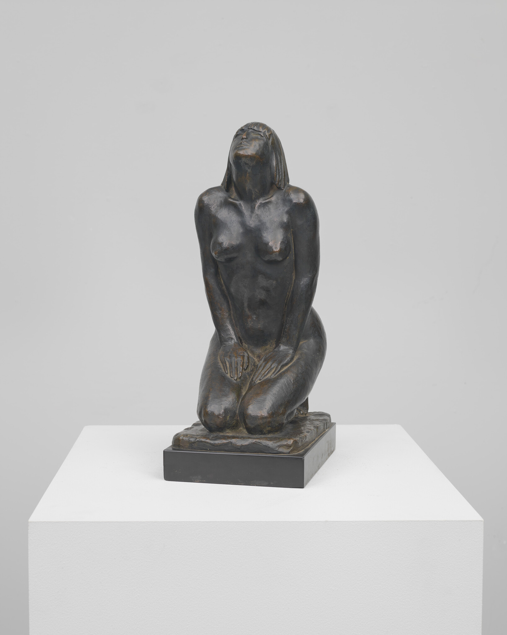 Bronze sculpture of a kneeling nude woman with hands on her thighs looking upward.