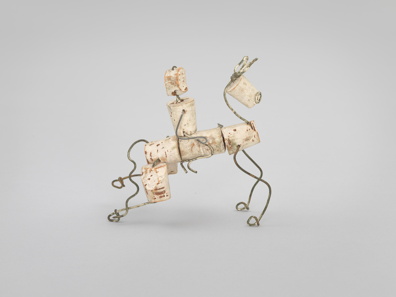 A small sculpture of a horse made from corks and wire, standing on a plain background.