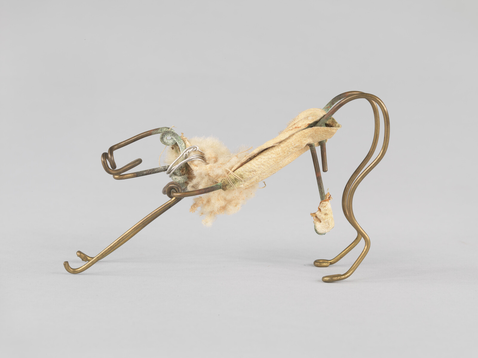 Small wire and fabric sculpture resembling an animal with bent brass legs and cotton stuffing.