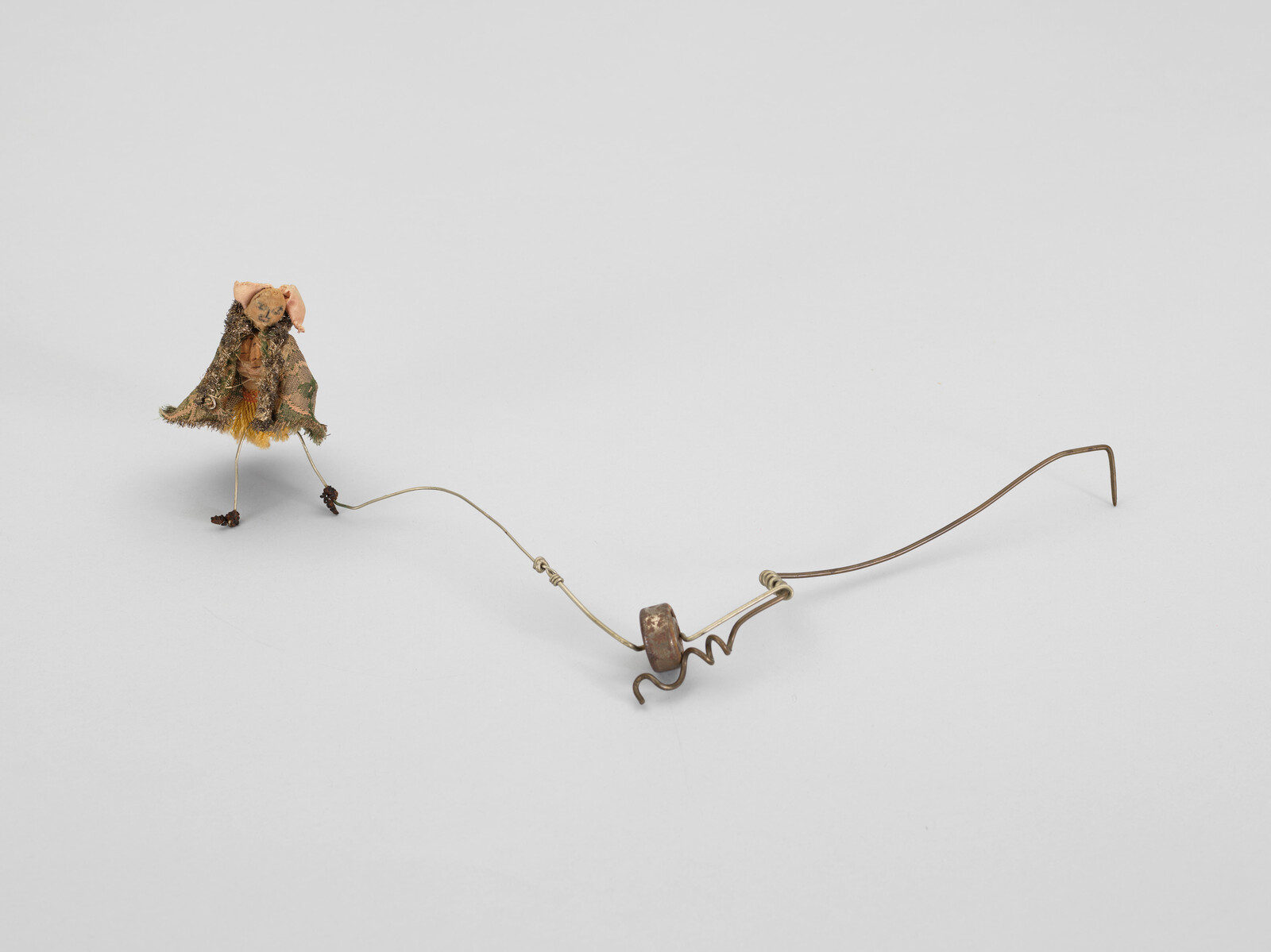 Small figure with a textured cloak connected to a wire structure on a plain background.