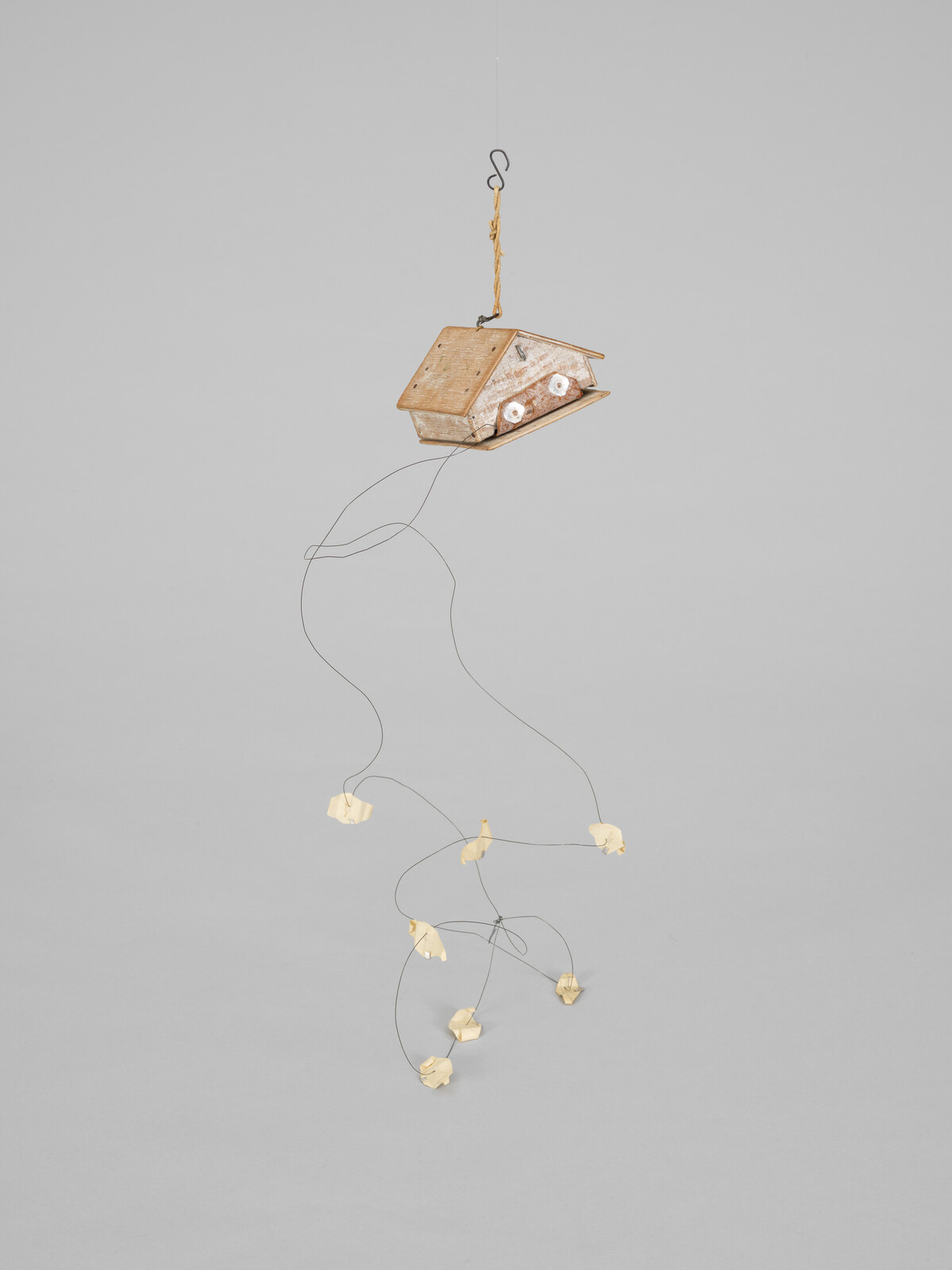 A small wooden birdhouse hangs from a cord with a delicate wire mobile of paper birds.