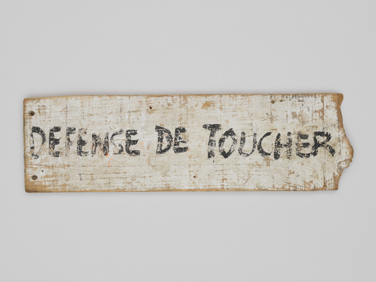 A worn wooden sign with French text "DEFENSE DE TOUCHER," meaning "Do Not Touch."