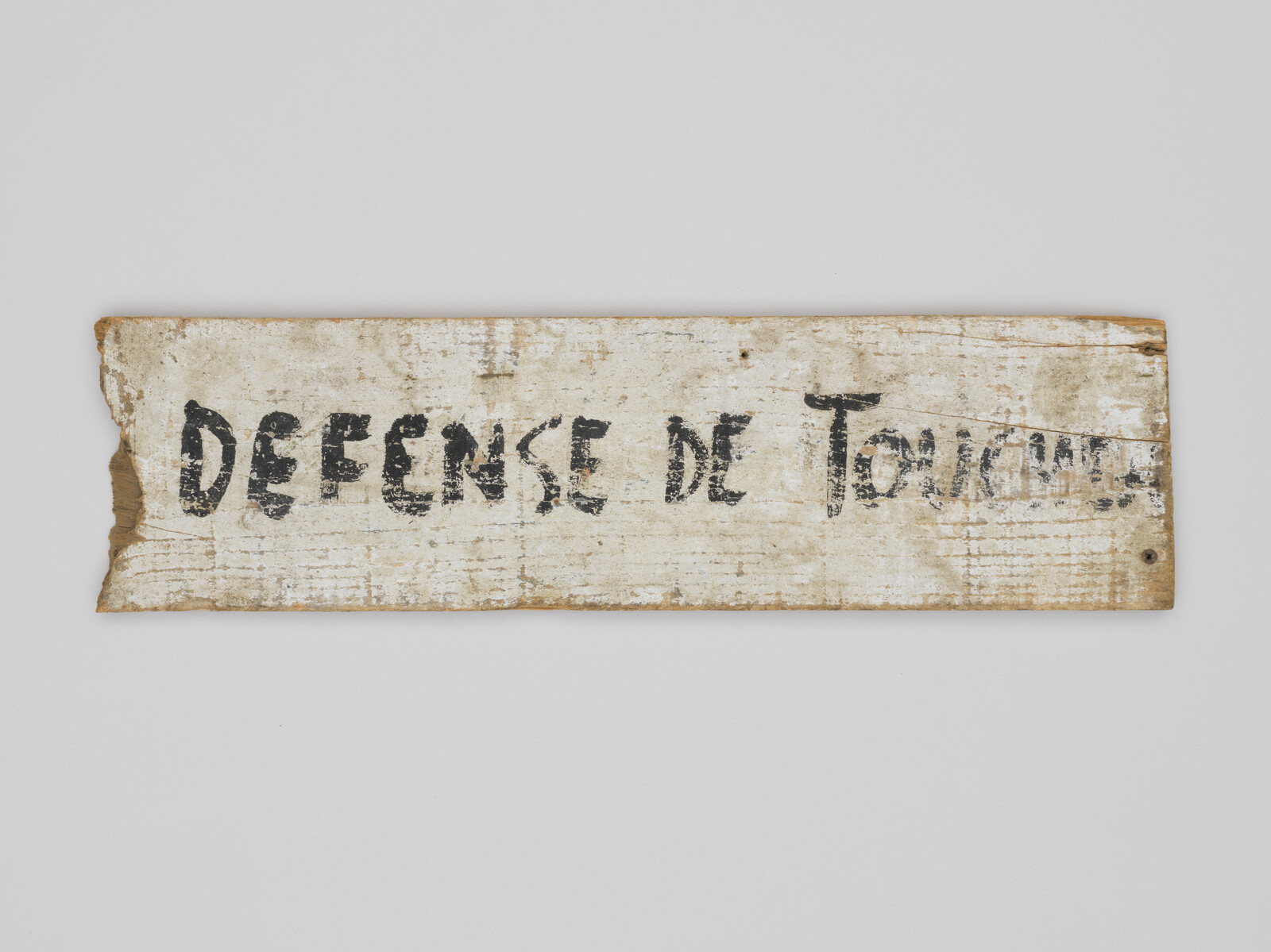 A worn wooden sign with the French words "DEFENSE DE TOUCHER," meaning "Do not touch."