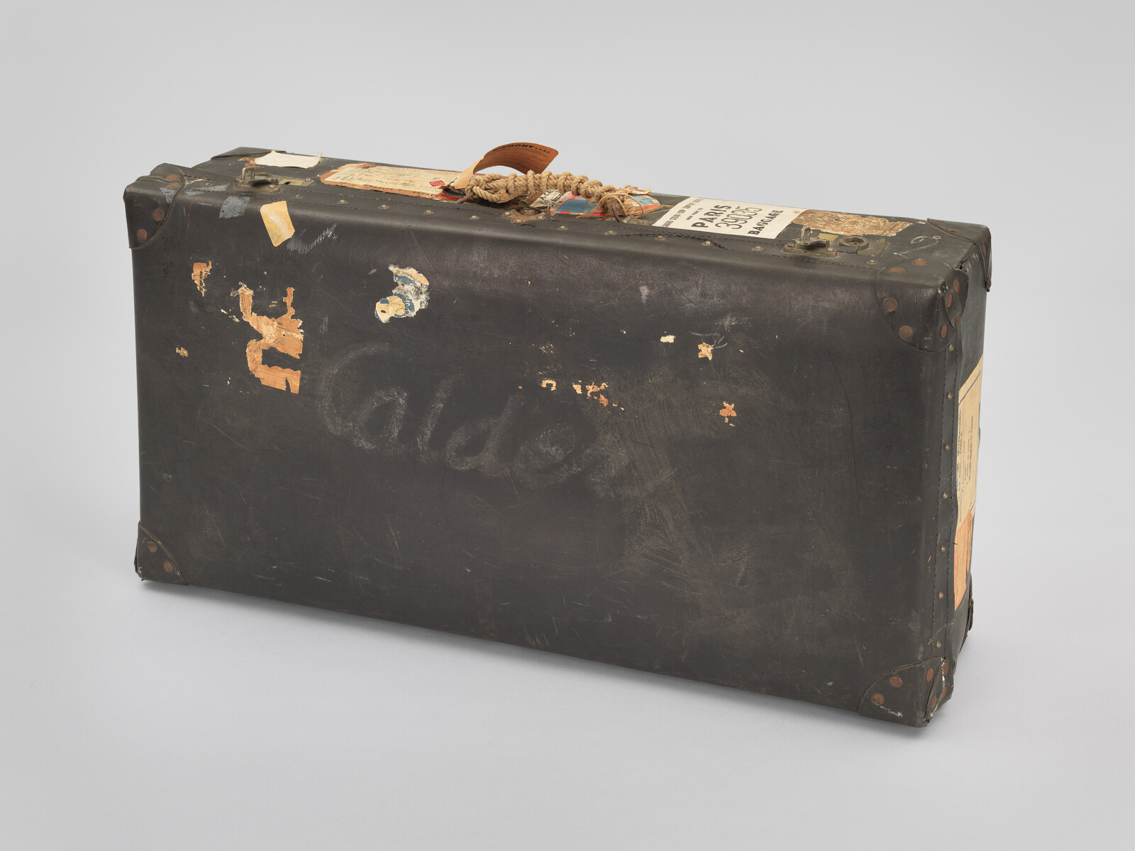 Worn black travel suitcase with scuffed corners, old labels, and a rope-tied leather handle.