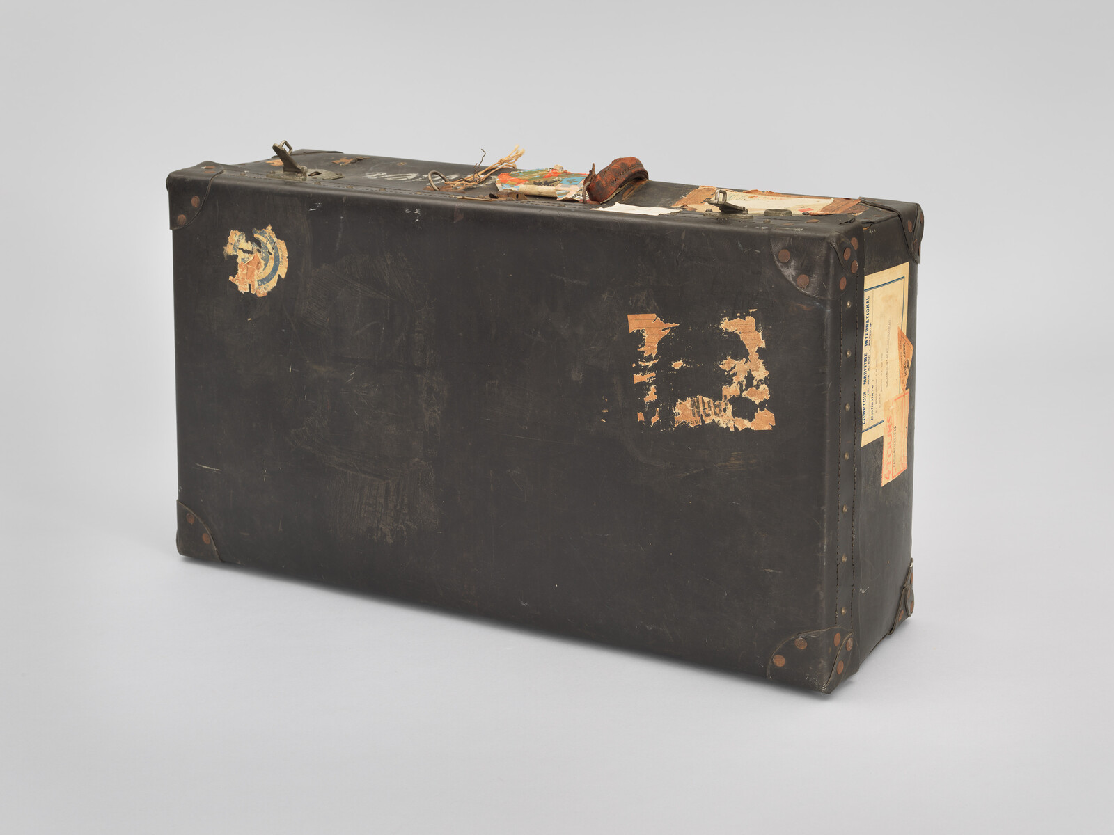 Worn black suitcase with old travel stickers and a damaged handle, showing signs of heavy use.