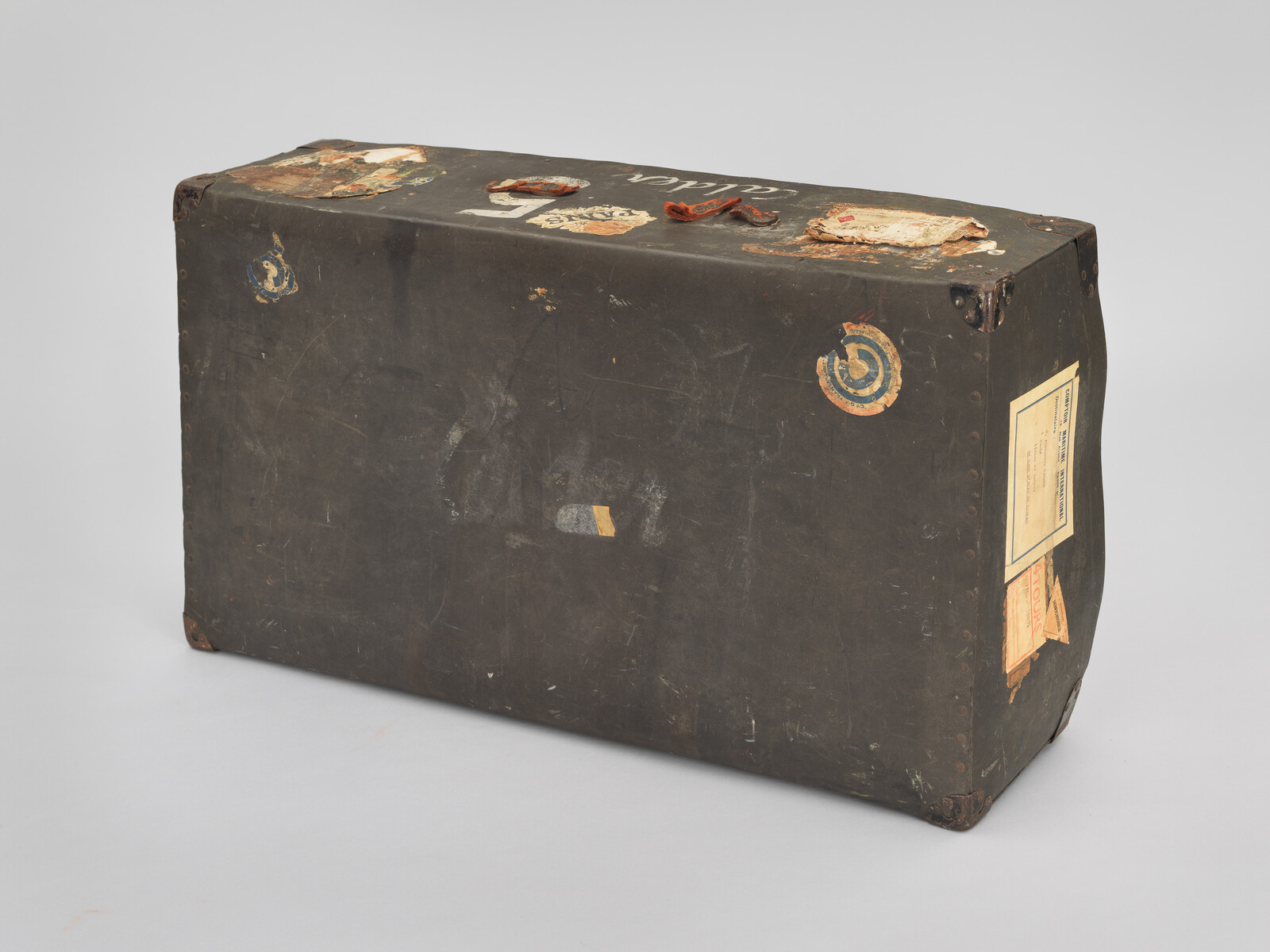 A worn black travel trunk with faded stickers, torn labels, and rusted metal corners.