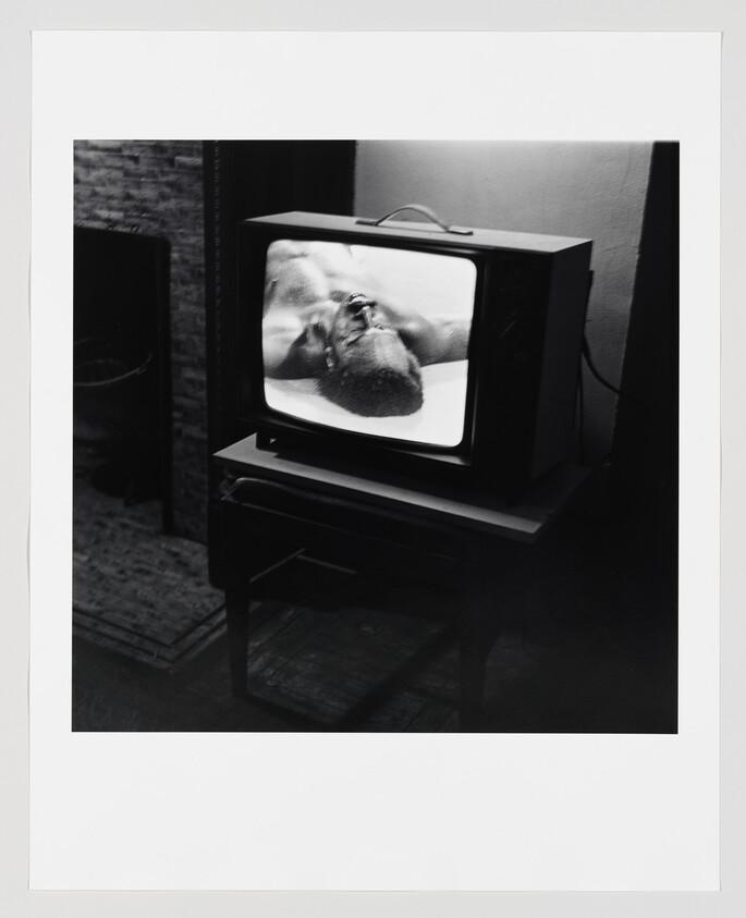 A vintage television shows a close-up of a man lying with his head tilted back.