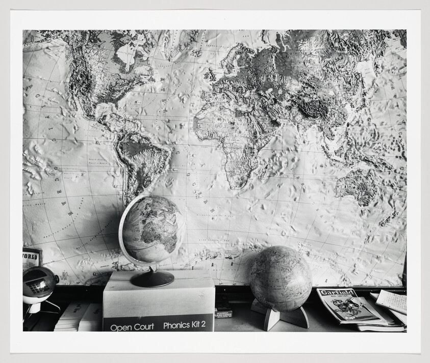 Large raised-relief world map on the wall with two globes on a desk below.