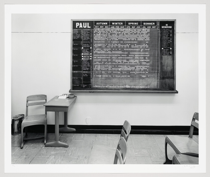 Large scheduling board labeled "PAUL" hangs above a small desk and empty chairs in a waiting room.