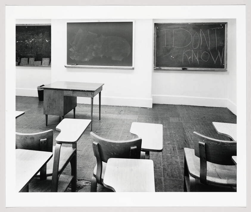 Empty classroom with scattered desks and a chalkboard reading "I don't know."