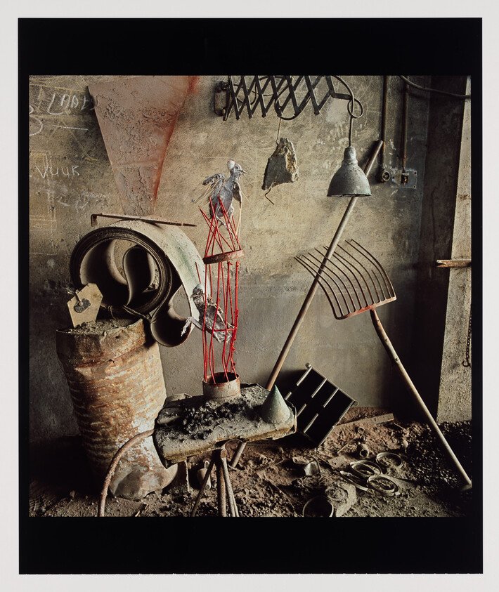 A cluttered workshop bench with a red wire sculpture holding two small birds and scattered tools.