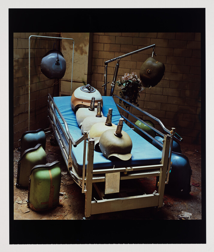 Hospital bed with five mannequin head molds lined up on blue mattress, surrounded by medical gear.