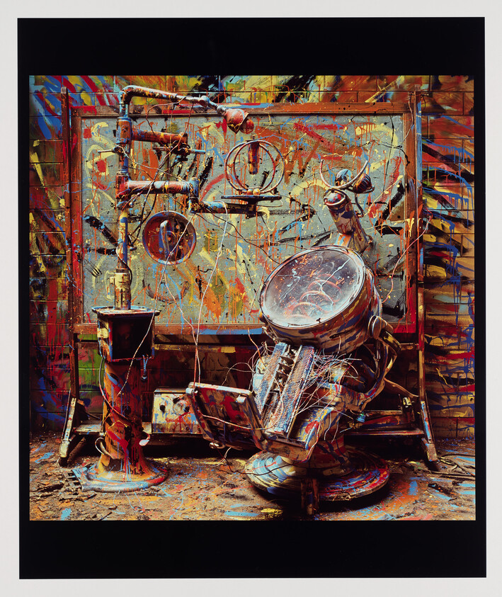 A paint-splattered mechanical contraption with wires, gauges, and a tilted round glass instrument.