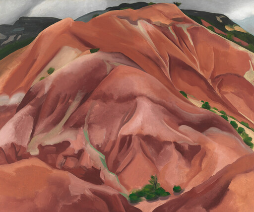 Red and orange hills with green shrubs, under a cloudy sky.