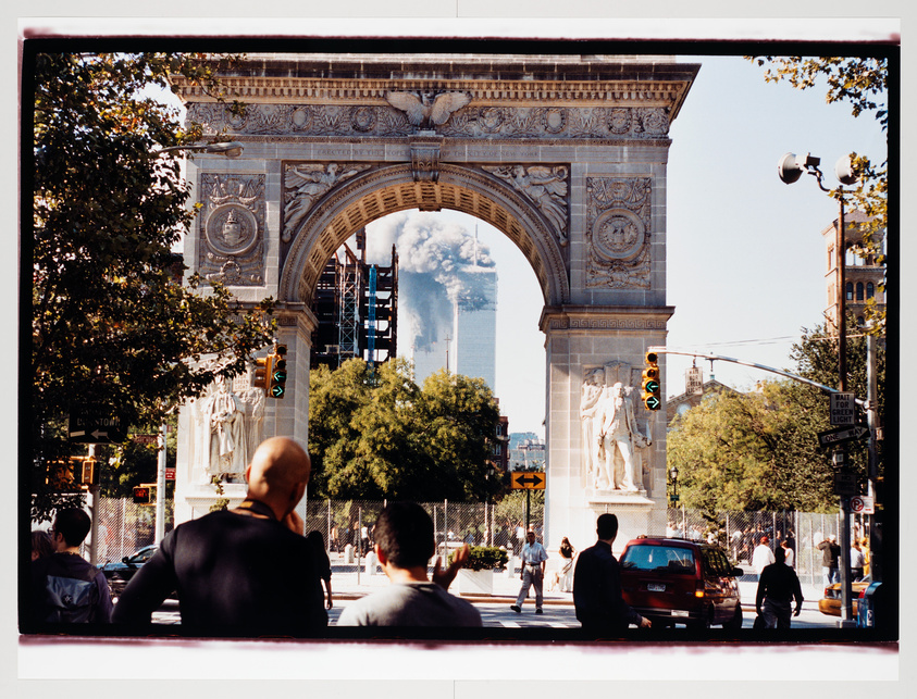 View through an arch with onlookers and smoke billowing from distant towers.