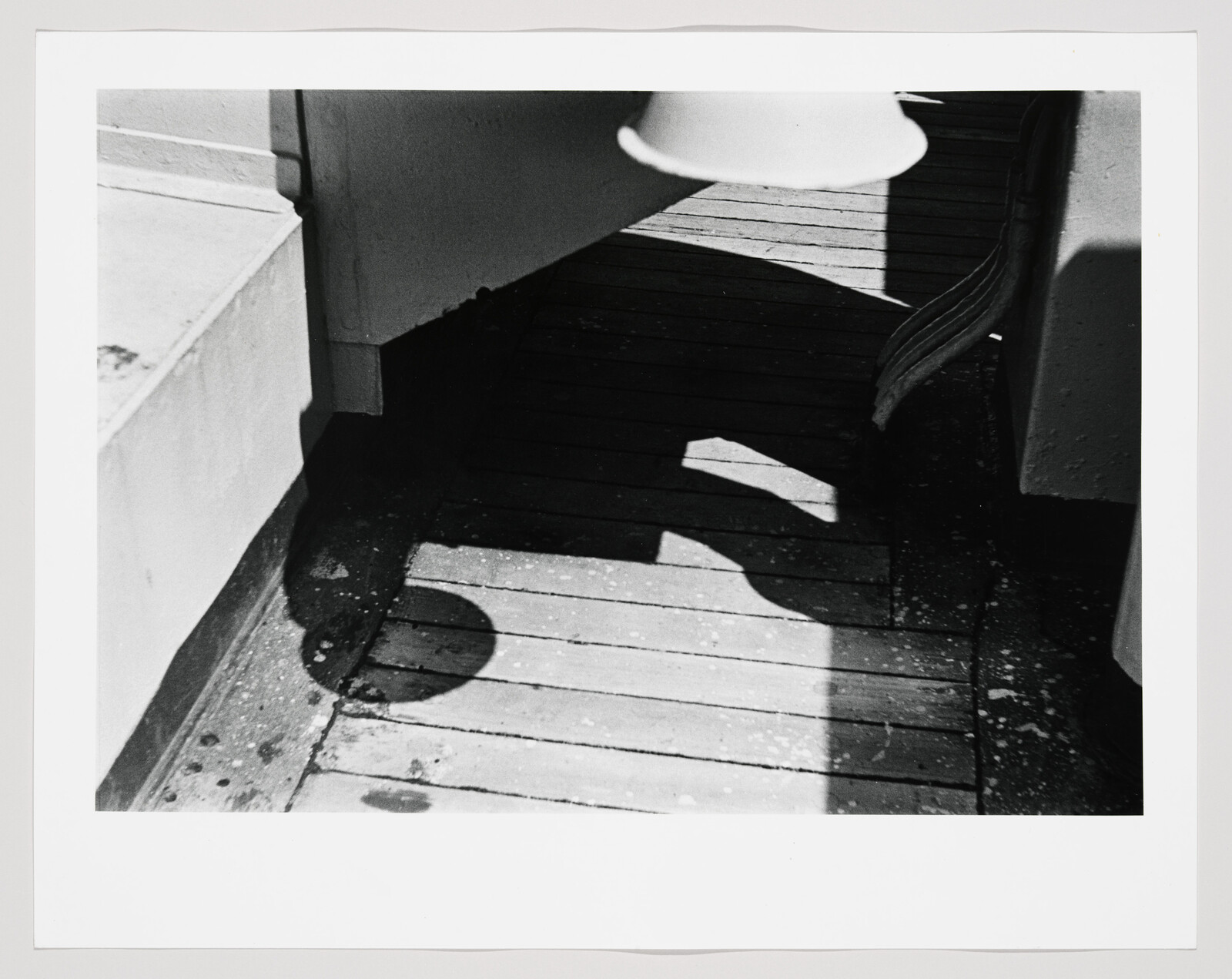 Sunlight casts curved lamp and railing shadows across a weathered wooden deck.