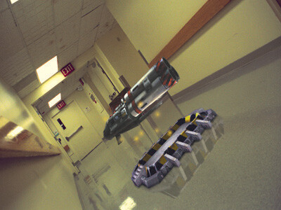 A futuristic hovering rifle floats in a hospital corridor above a circular metallic device on the floor.