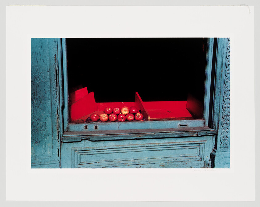 Red apples arranged on a blue shop window ledge inside a red display box.