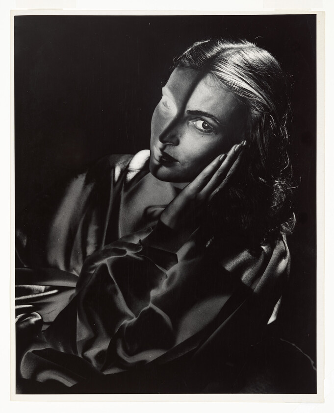 Woman with hand on her face looks toward camera as dramatic shadow crosses her face.