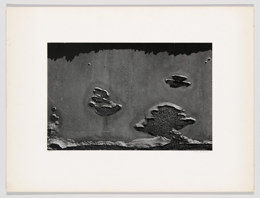 Peeling paint and rust patches create irregular island-like shapes on a dark metal surface.