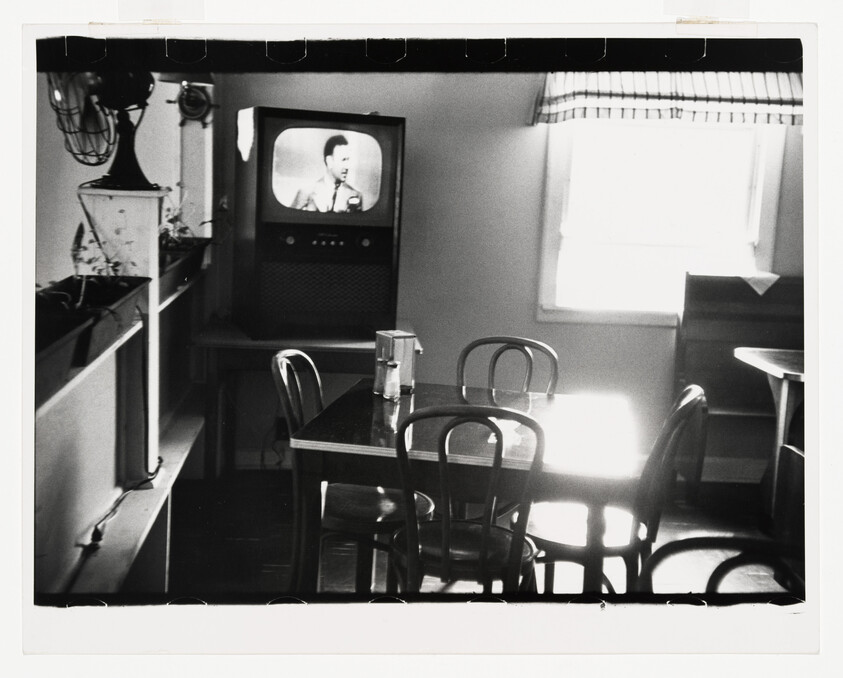 Empty diner dining table and chairs with a small television showing a man in the background.