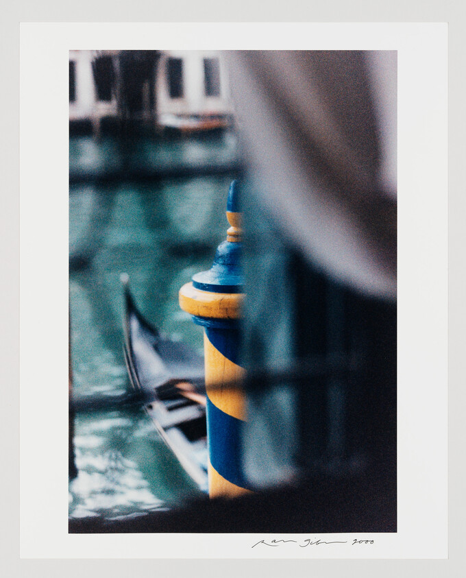 Blue and yellow striped mooring pole beside a blurred gondola on a Venetian canal.