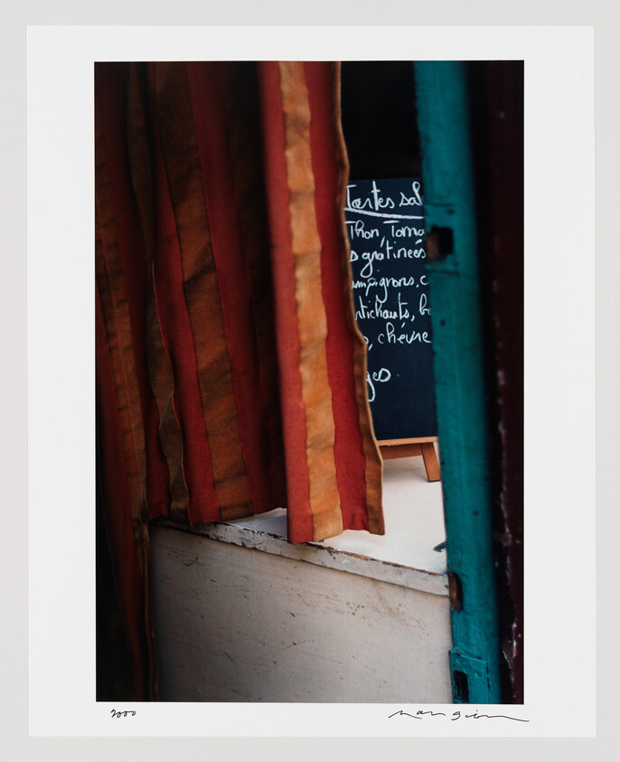 Striped red and orange curtain partly open revealing a chalkboard menu behind a turquoise doorframe.