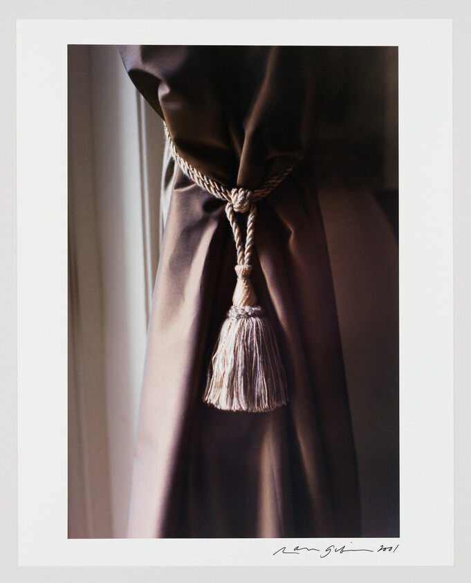A tasseled rope tieback holds a brown curtain closed beside a window.