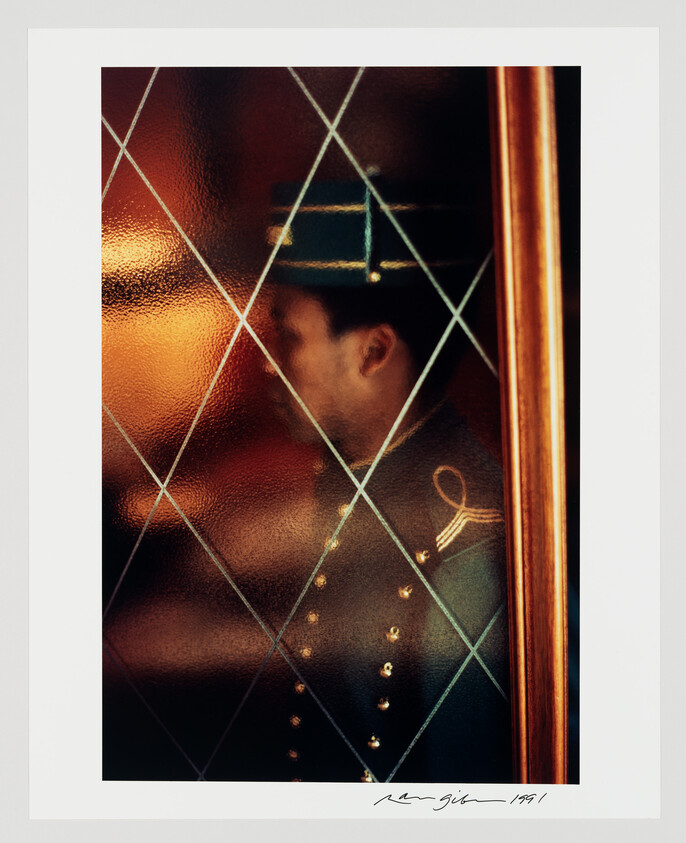 Hotel bellhop in uniform standing behind diamond-patterned frosted glass door.