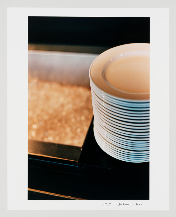 A tall stack of white plates sits next to a bin of crushed ice on a counter.