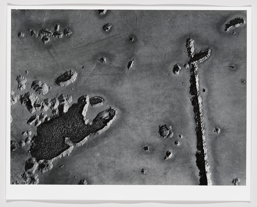 Aerial black-and-white view of a cratered lunar-like surface with a long trench and scattered craters.