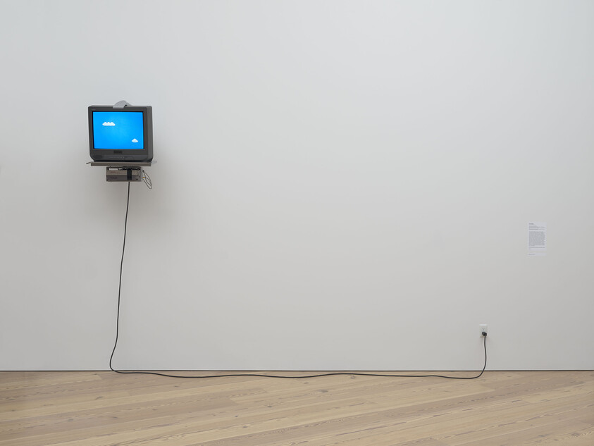 A small TV mounted on a wall shows a blue screen with two white clouds, plugged in below.