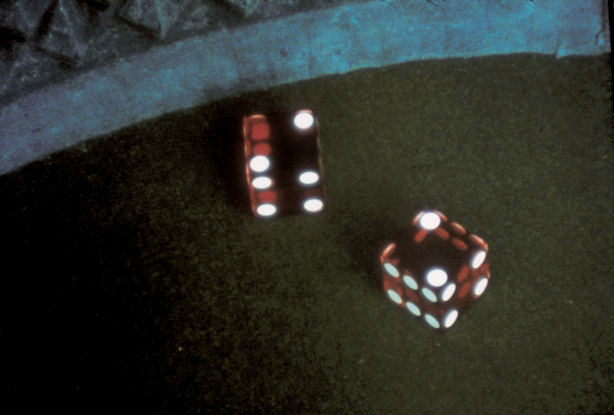 Two red dice rest on a dark felt table, one die showing three pips on top.