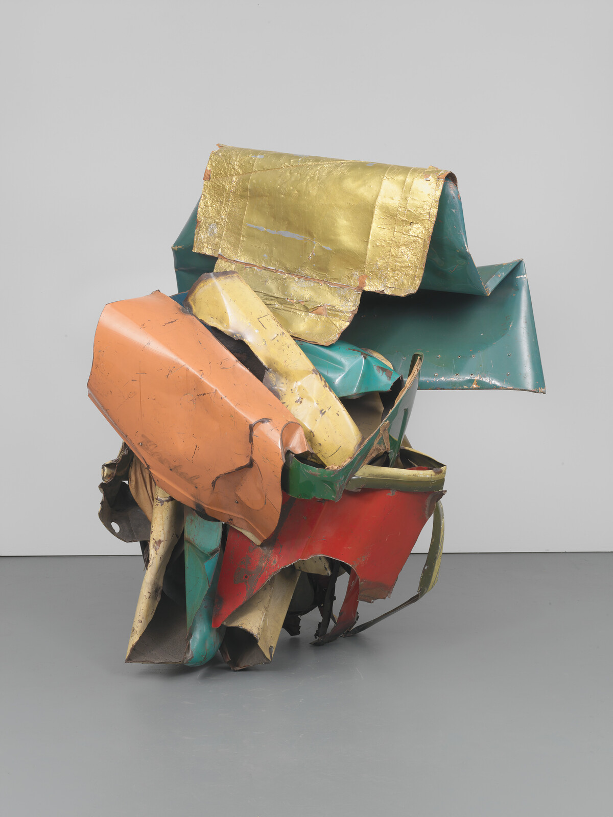 Crushed painted metal sheets assembled into a colorful abstract sculpture resting on a gallery floor.