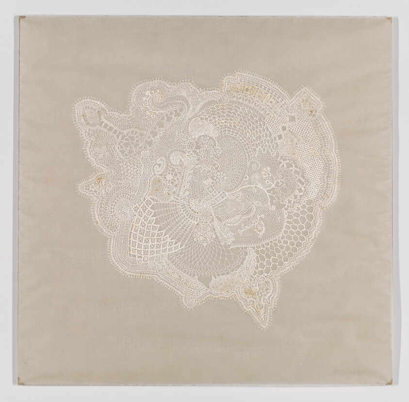 A delicate piece of white lace with intricate patterns is centered on a beige fabric background, creating a contrast that highlights the detailed craftsmanship of the lacework.