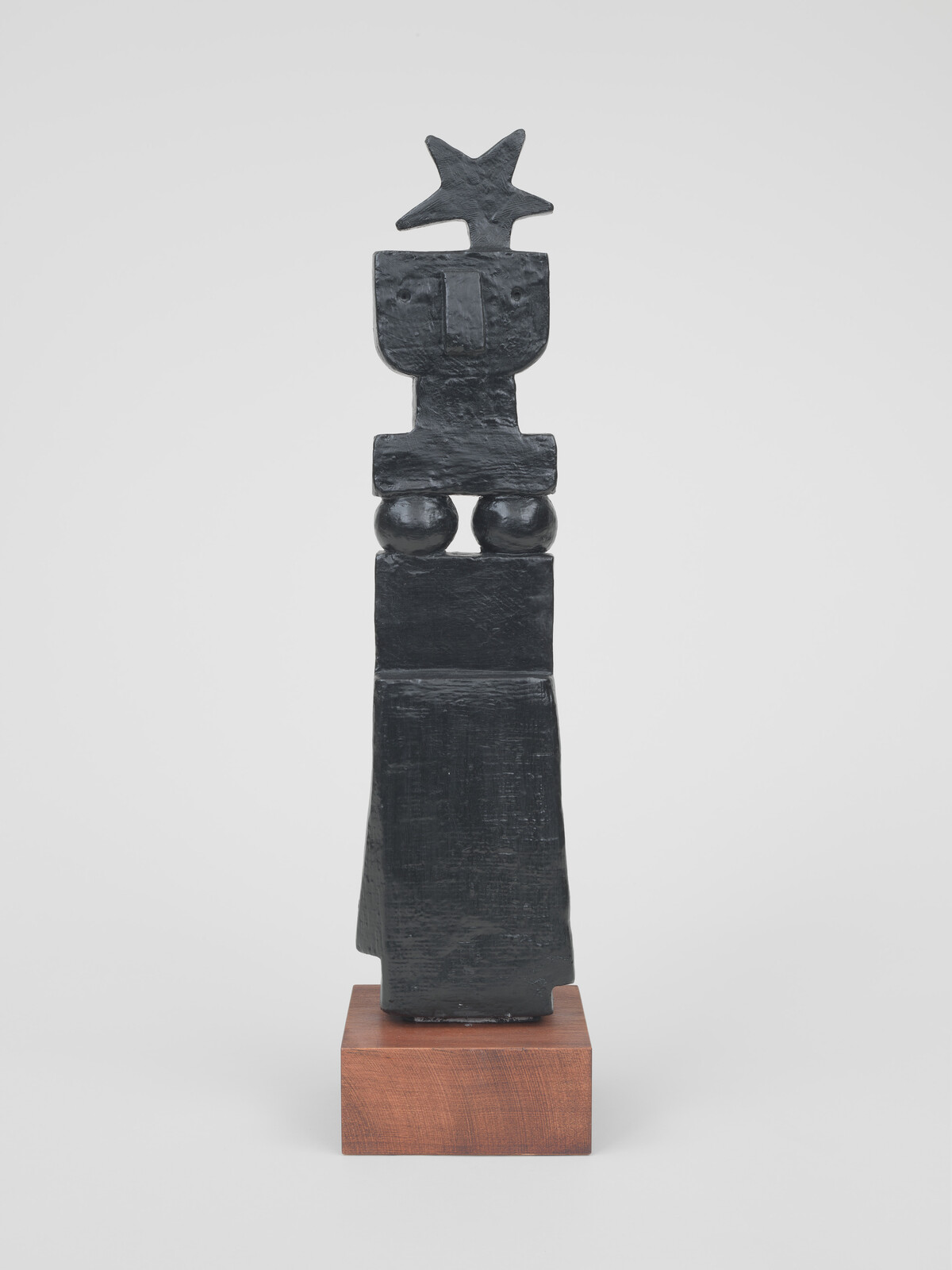 A tall black abstract wooden sculpture with a star-shaped top standing on a square base.