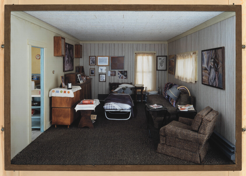 A modest living room with a fold-out bed, armchair, couch, and framed pictures on the walls.