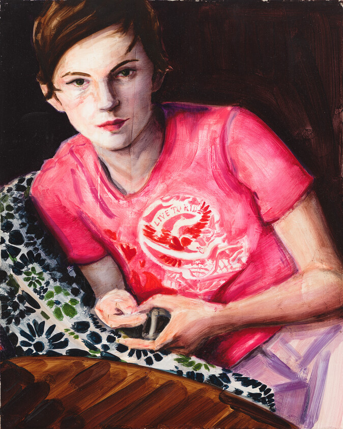 Young person in a bright pink shirt holding a small device while sitting at a patterned table.