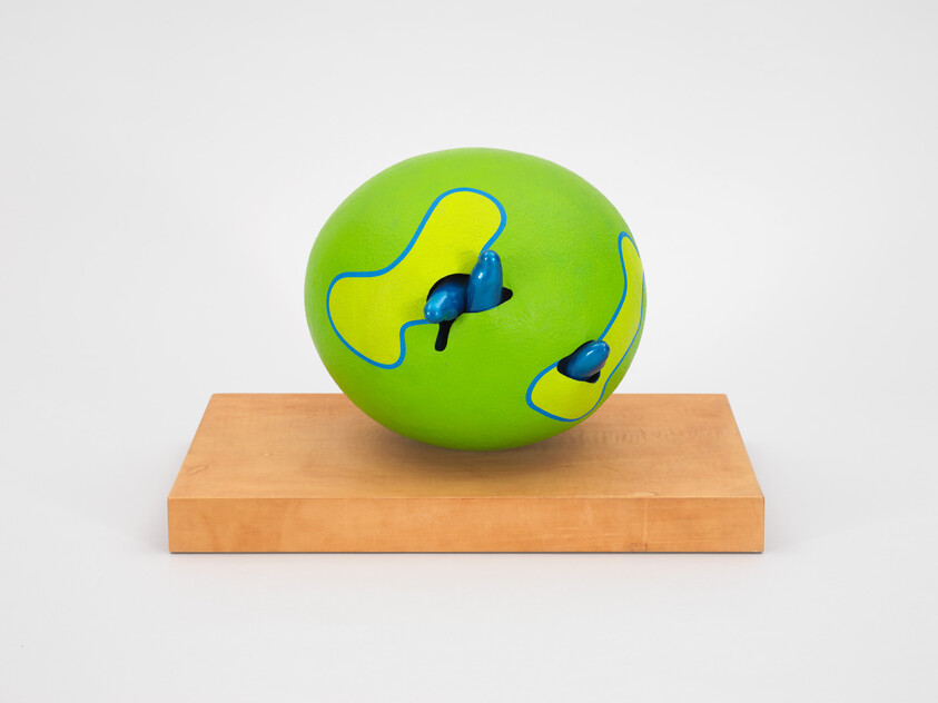 Green sphere with blue abstract shapes on a wooden platform, displayed on a white pedestal.