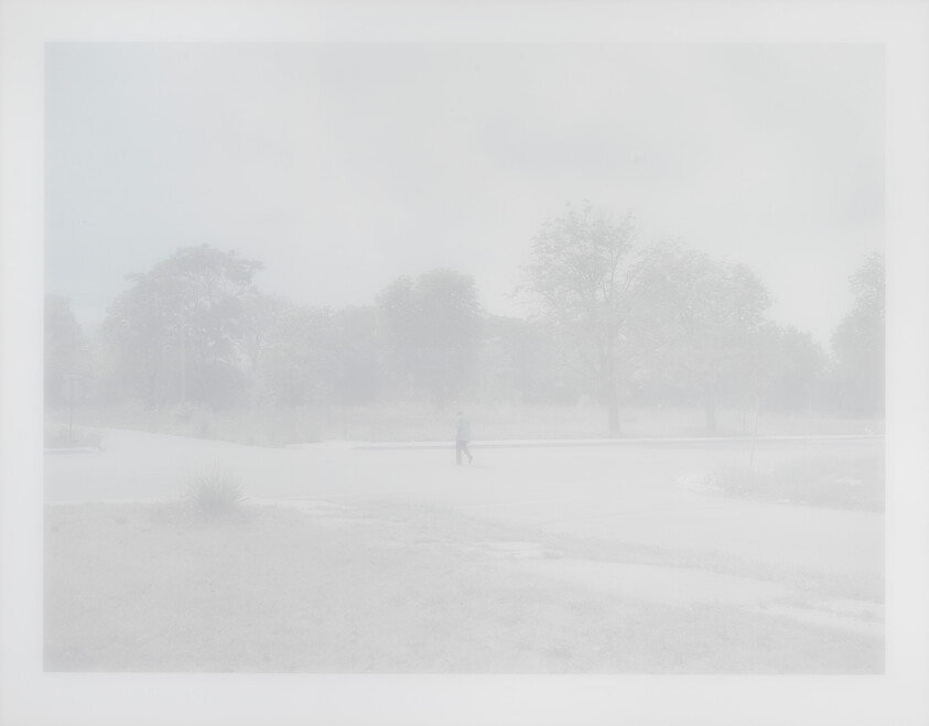 A solitary person walks along a foggy road with faint trees in the background.