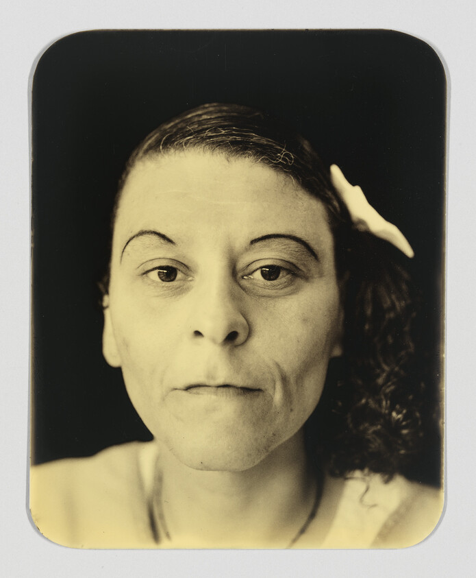 A woman with arched eyebrows and a white hair clip looks directly at the camera.