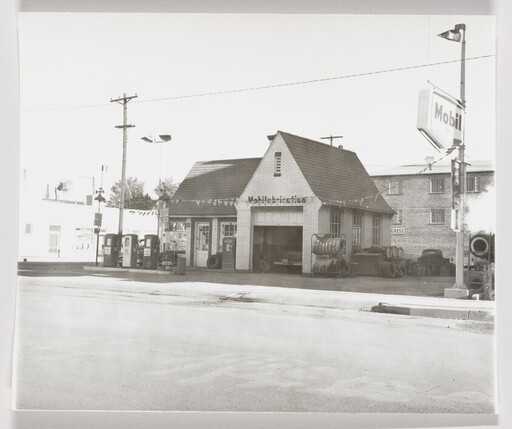A vintage Mobil gas station with fuel pumps, stacked tires, and a garage bay.