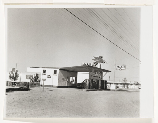 A vintage Mobil gas station with Pegasus sign and fuel pumps on a quiet dusty street.